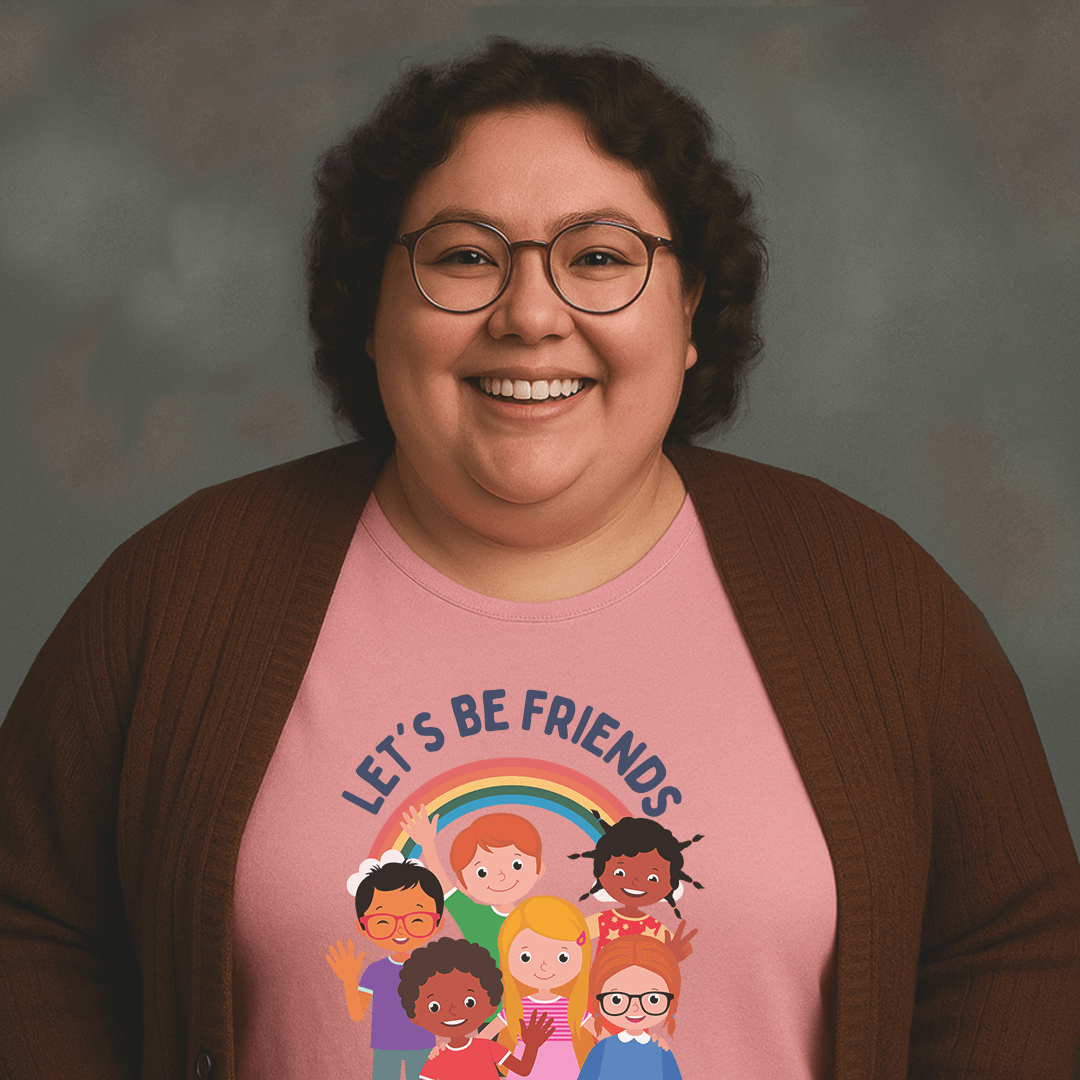 Smiling woman with curly hair and glasses wearing a pink t-shirt that says ‘LET’S BE FRIENDS’ with an illustration of diverse children standing under a rainbow