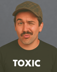 Man with mustache and cap winking while wearing a black “TOXIC” t-shirt, looking playful.