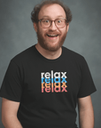 Smiling man with glasses and beard wearing a black Milk Sandwich t-shirt featuring a colorful stacked relax design in white, blue, orange, and pink text.
