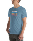 Side view of a man wearing a Milk Sandwich steel blue t-shirt featuring a stacked relax text design in distressed white, blue, orange, and pink colors.