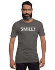 Man wearing a asphalt Milk Sandwich t-shirt with the word "SMILE!" in bold, distressed white lettering across the chest, standing confidently against a plain background.