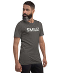Side-facing man wearing asphalt Milk Sandwich t-shirt with distressed white text that reads SMILE! on the chest, set against a white backdrop.