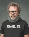 Man with serious expression wearing glasses and a black Milk Sandwich T-shirt  that says "SMILE!" in bold white letters.
