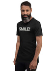 Man in a black Milk Sandwich t-shirt featuring the word "SMILE!" in bold, distressed white letters, posing confidently with a slight turn against a white background.