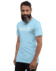 Man in a ocean blue Milk Sandwich t-shirt featuring the word "SMILE!" in bold, distressed white letters, posing confidently with a slight turn against a white background.