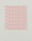 Close-up of silver t-shirt fabric with bold red “TRIGGERED” text repeated in stacked rows.          