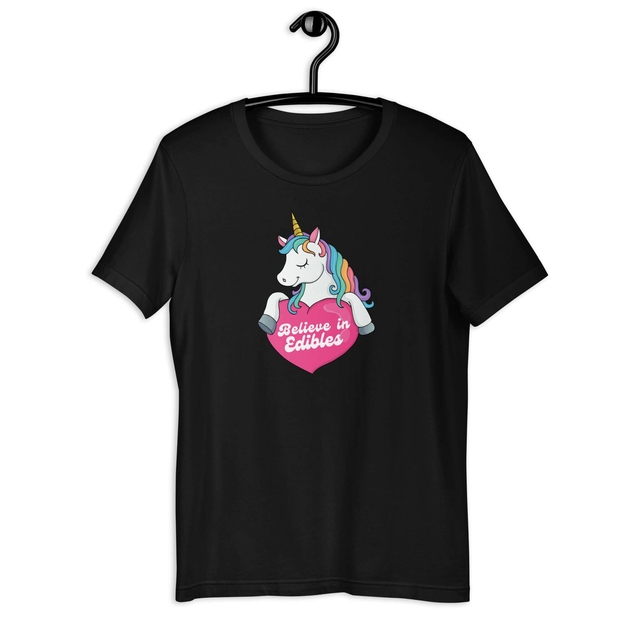 Black t-shirt on a hanger with a colorful unicorn graphic above a pink heart that says “Believe in Edibles.”