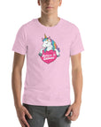 Man wearing a lilac t-shirt with a colorful unicorn holding a pink heart that says “Believe in Edibles,” standing facing forward with one hand relaxed and the other in his pocket.          