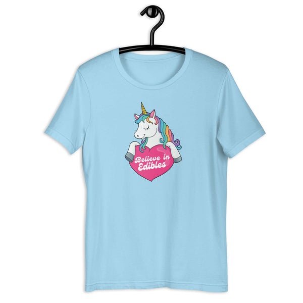 Ocean Blue t-shirt on a hanger with a colorful unicorn graphic above a pink heart that says “Believe in Edibles.”