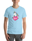 Man wearing a ocean blue t-shirt with a colorful unicorn holding a pink heart that says “Believe in Edibles,” standing facing forward with one hand relaxed and the other in his pocket.          