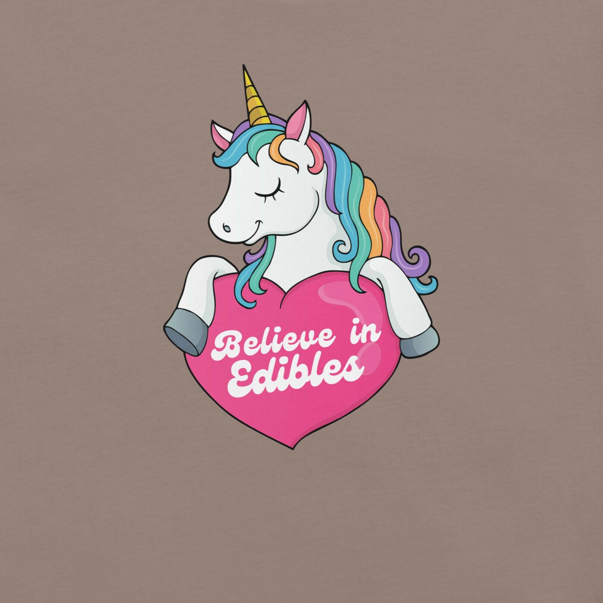 Close-up of a colorful unicorn graphic holding a pink heart with the text “Believe in Edibles” on a pebble fabric background.