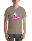 Man wearing a pebble t-shirt with a colorful unicorn holding a pink heart that says “Believe in Edibles,” standing facing forward with one hand relaxed and the other in his pocket.          