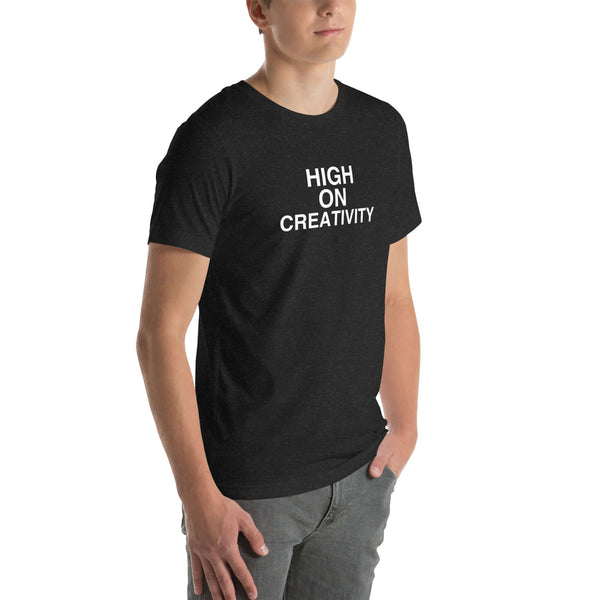 Young man wearing a black t-shirt with white text ‘HIGH ON CREATIVITY’, standing angled to the side with hands in pockets.