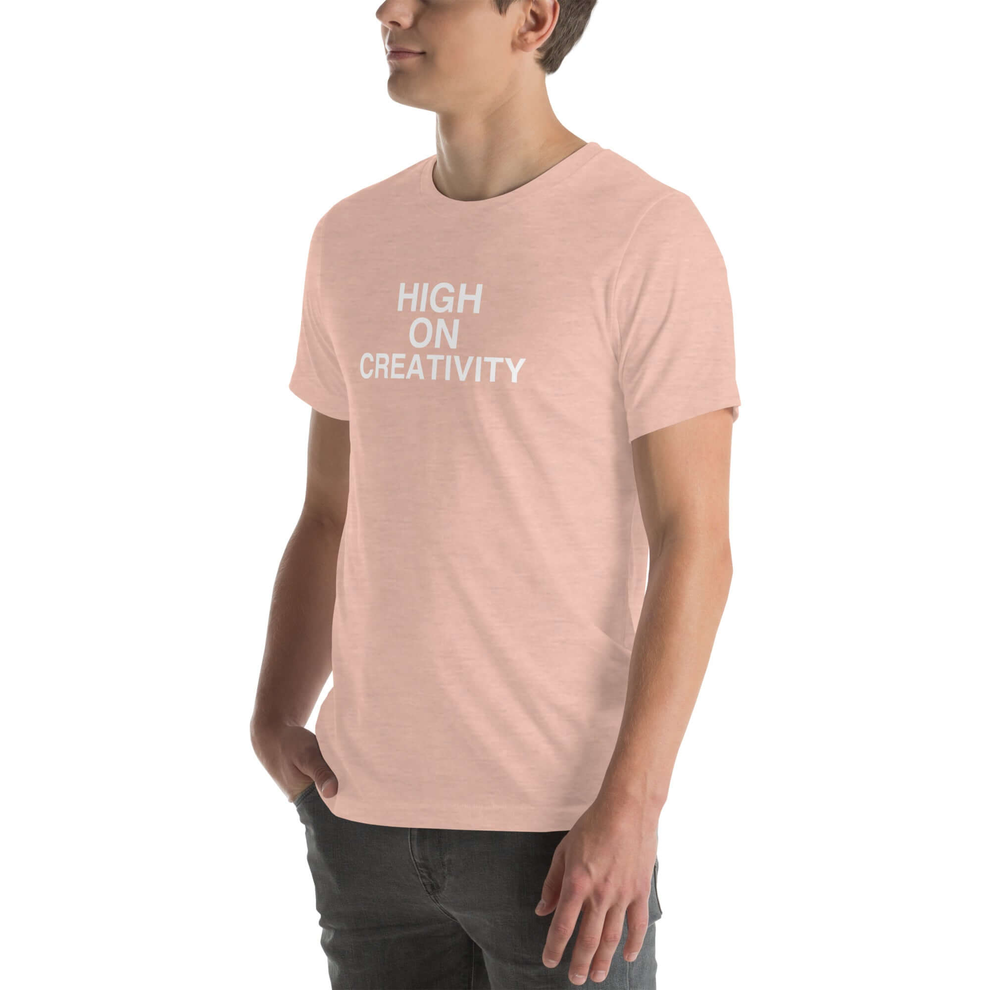 Man wearing a peach t-shirt with white text ‘HIGH ON CREATIVITY’, standing sideways with one hand in pocket