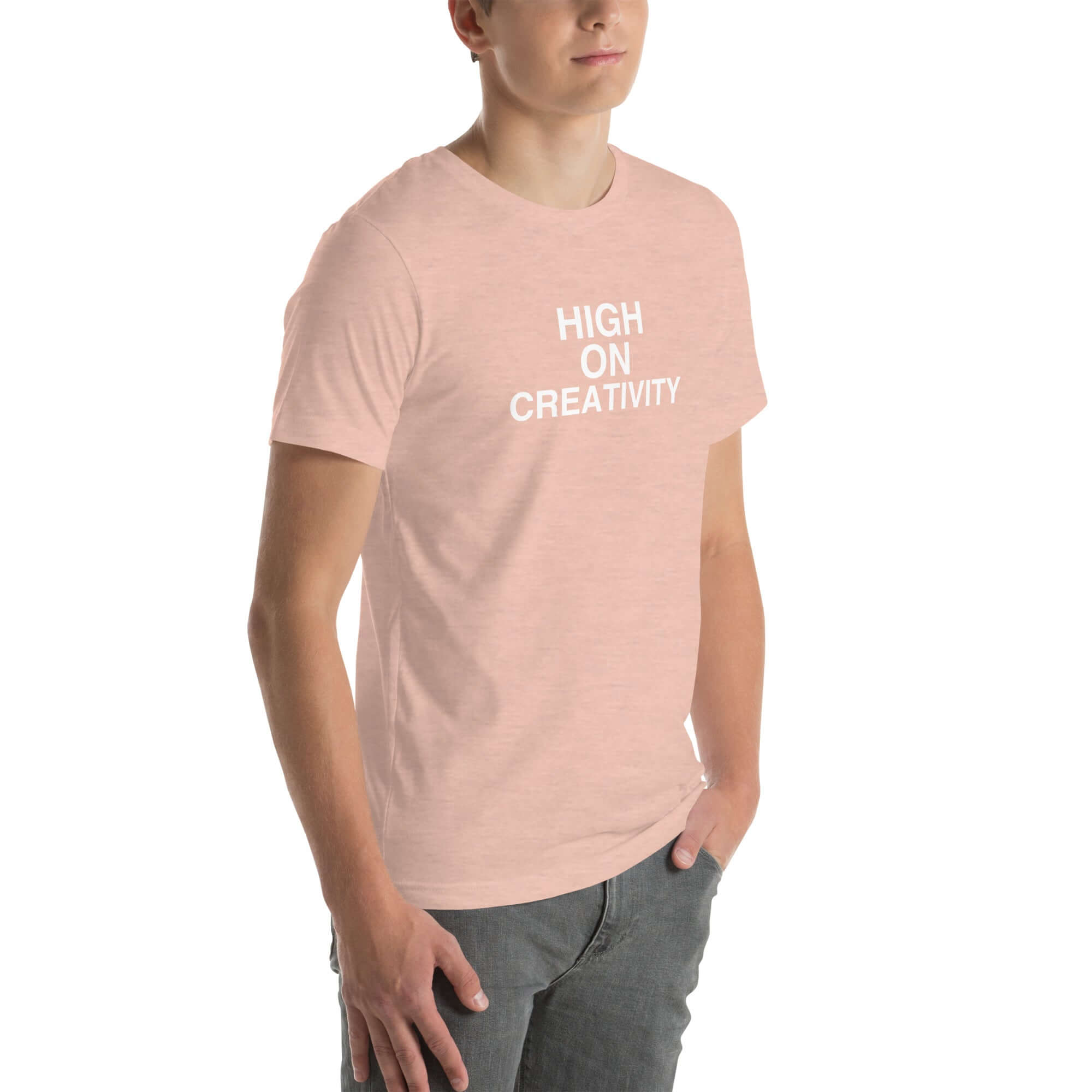 Young man wearing a peach t-shirt with white text ‘HIGH ON CREATIVITY’, standing angled to the side with hands in pockets.