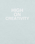 Close-up of ice blue t-shirt fabric with the phrase “HIGH ON CREATIVITY” printed in bold white uppercase letters in three lines.