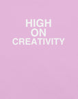Close-up of Lilac t-shirt fabric with the phrase “HIGH ON CREATIVITY” printed in bold white uppercase letters in three lines.
