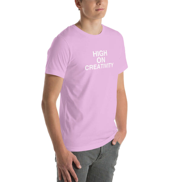 Young man wearing a lilac t-shirt with white text ‘HIGH ON CREATIVITY’, standing angled to the side with hands in pockets.