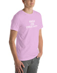 Young man wearing a lilac t-shirt with white text ‘HIGH ON CREATIVITY’, standing angled to the side with hands in pockets.
