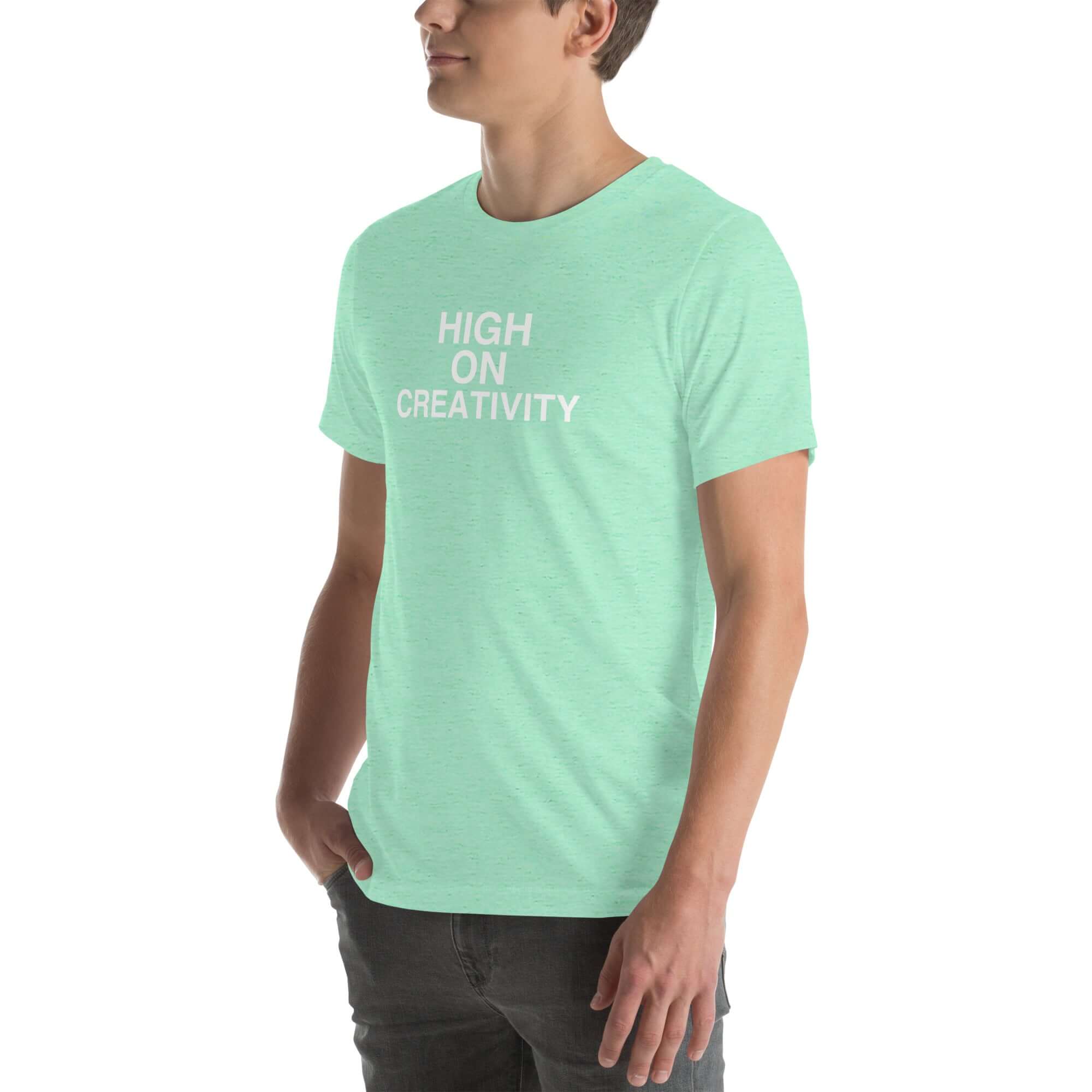 Man wearing a mint t-shirt with white text ‘HIGH ON CREATIVITY’, standing sideways with one hand in pocket