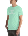 Man wearing a mint t-shirt with white text ‘HIGH ON CREATIVITY’, standing sideways with one hand in pocket