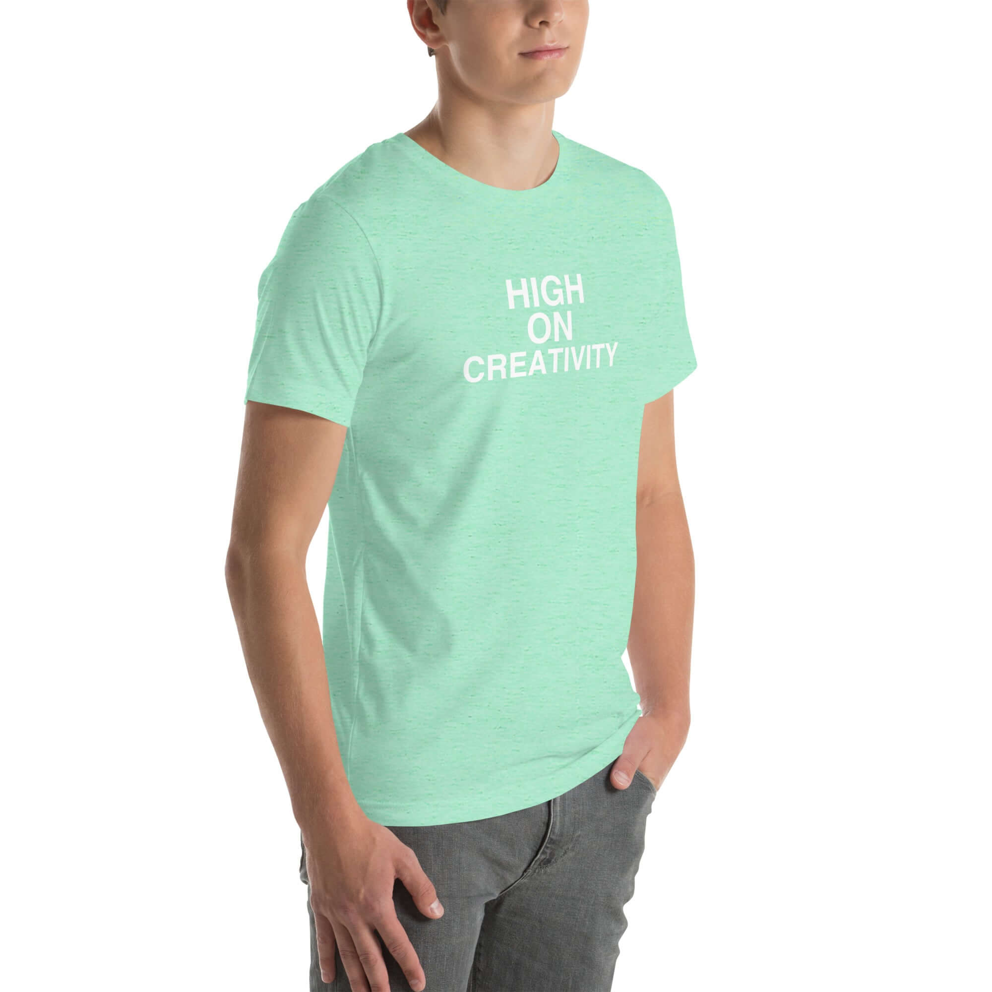 Young man wearing a mint t-shirt with white text ‘HIGH ON CREATIVITY’, standing angled to the side with hands in pockets.
