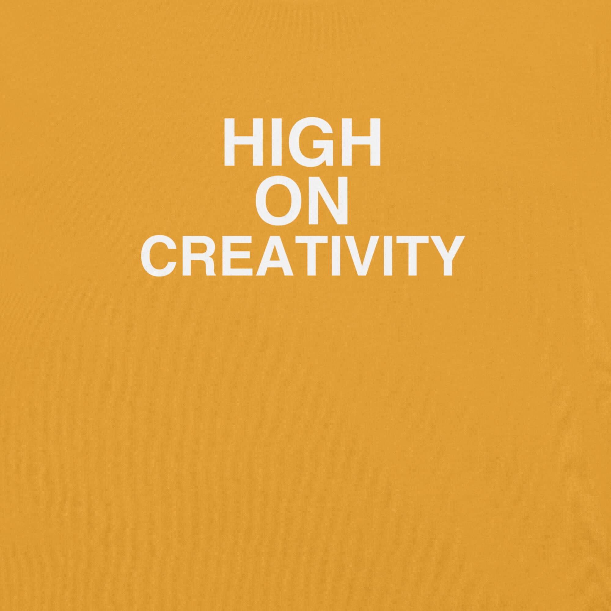 Close-up of mustard t-shirt fabric with the phrase “HIGH ON CREATIVITY” printed in bold white uppercase letters in three lines.