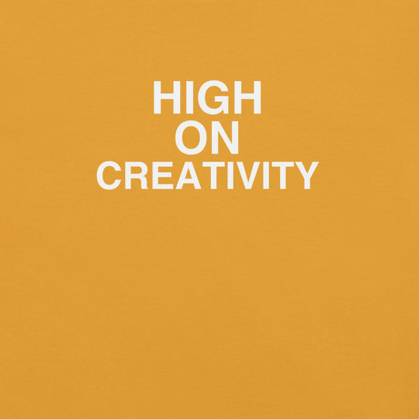 Close-up of mustard t-shirt fabric with the phrase “HIGH ON CREATIVITY” printed in bold white uppercase letters in three lines.
