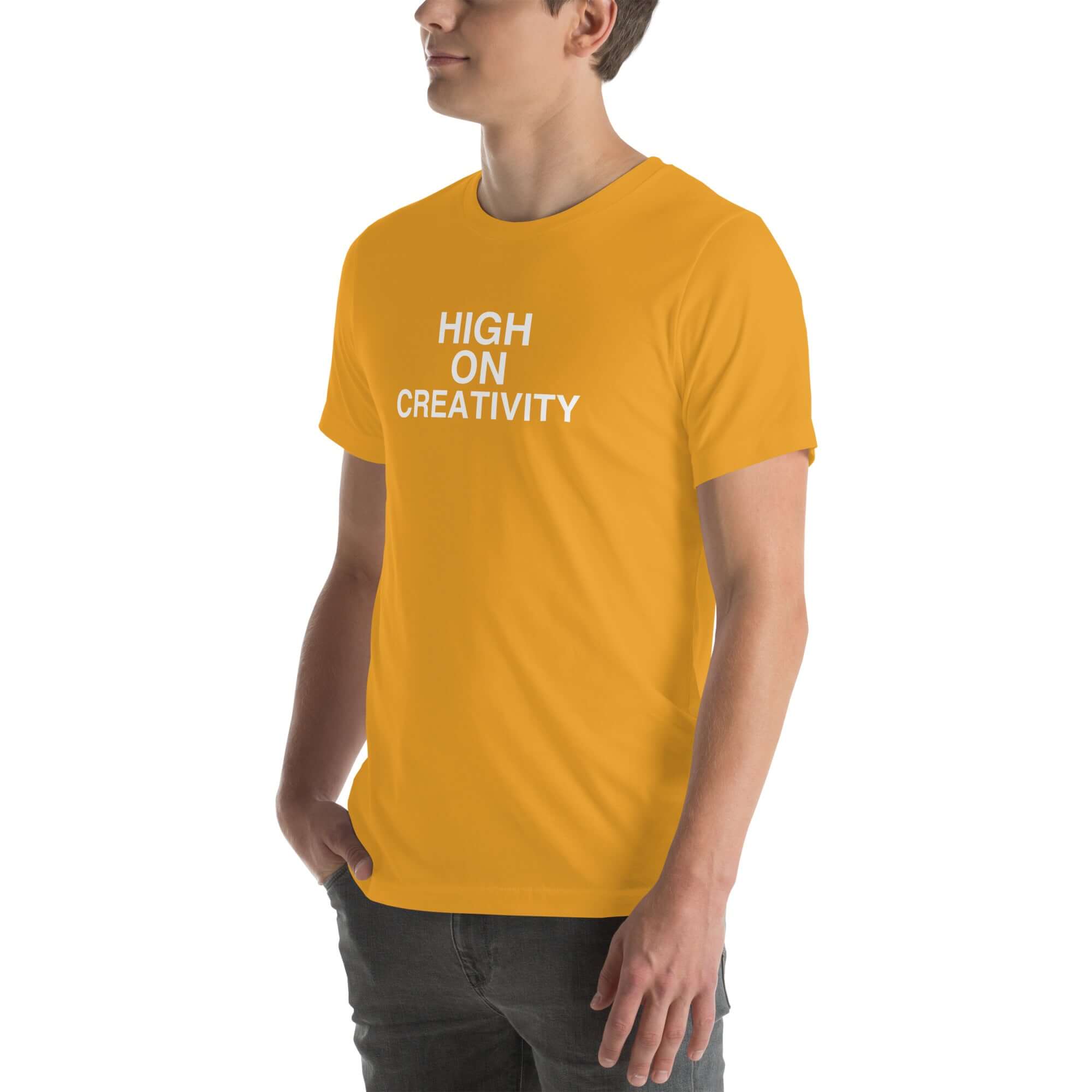 Man wearing a mustard t-shirt with white text ‘HIGH ON CREATIVITY’, standing sideways with one hand in pocket