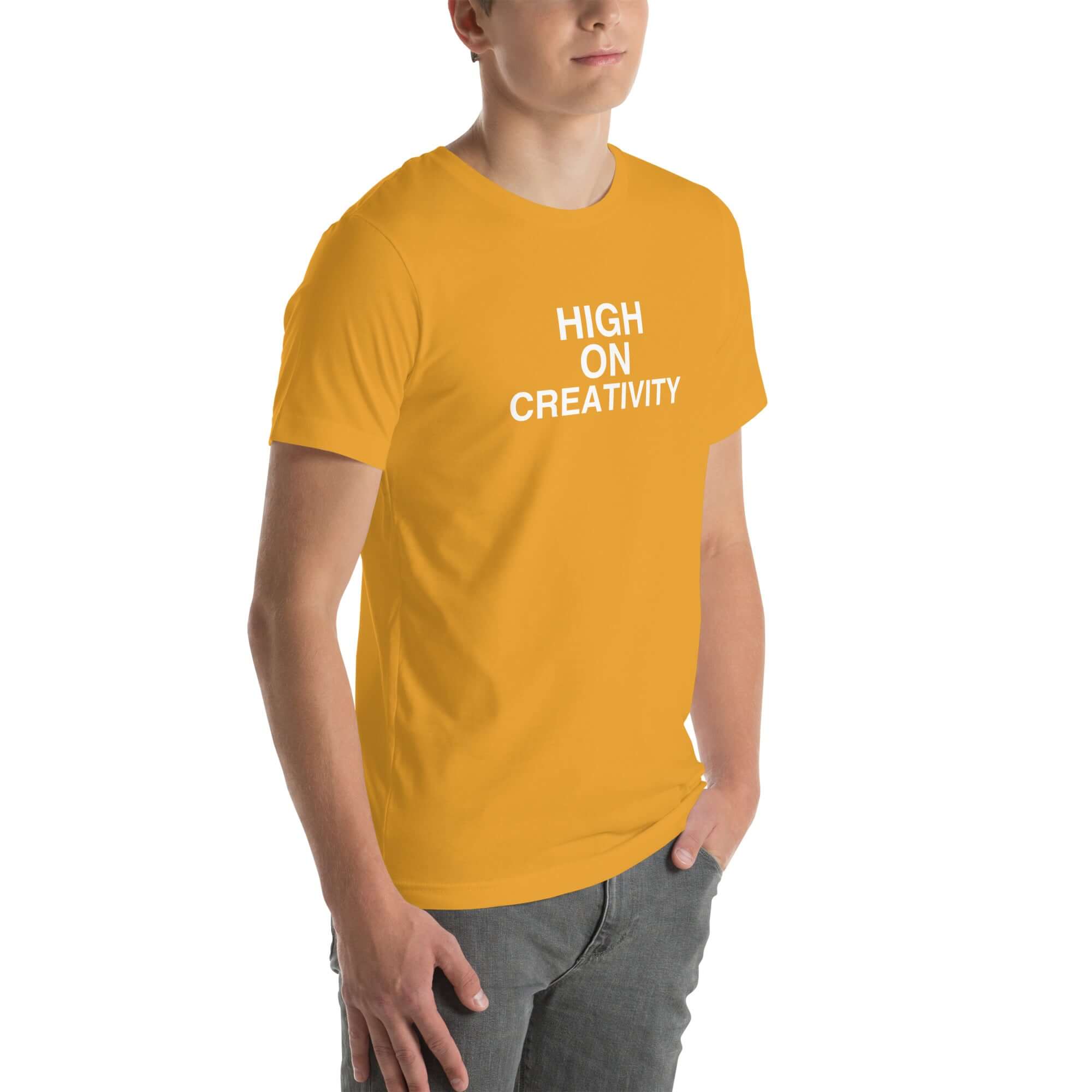 Young man wearing a mustard t-shirt with white text ‘HIGH ON CREATIVITY’, standing angled to the side with hands in pockets.