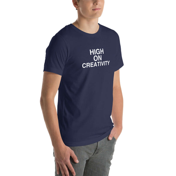 Young man wearing a navy t-shirt with white text ‘HIGH ON CREATIVITY’, standing angled to the side with hands in pockets.