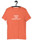Orange t-shirt on a hanger with the phrase “HIGH ON CREATIVITY” printed in white, centered on the chest.