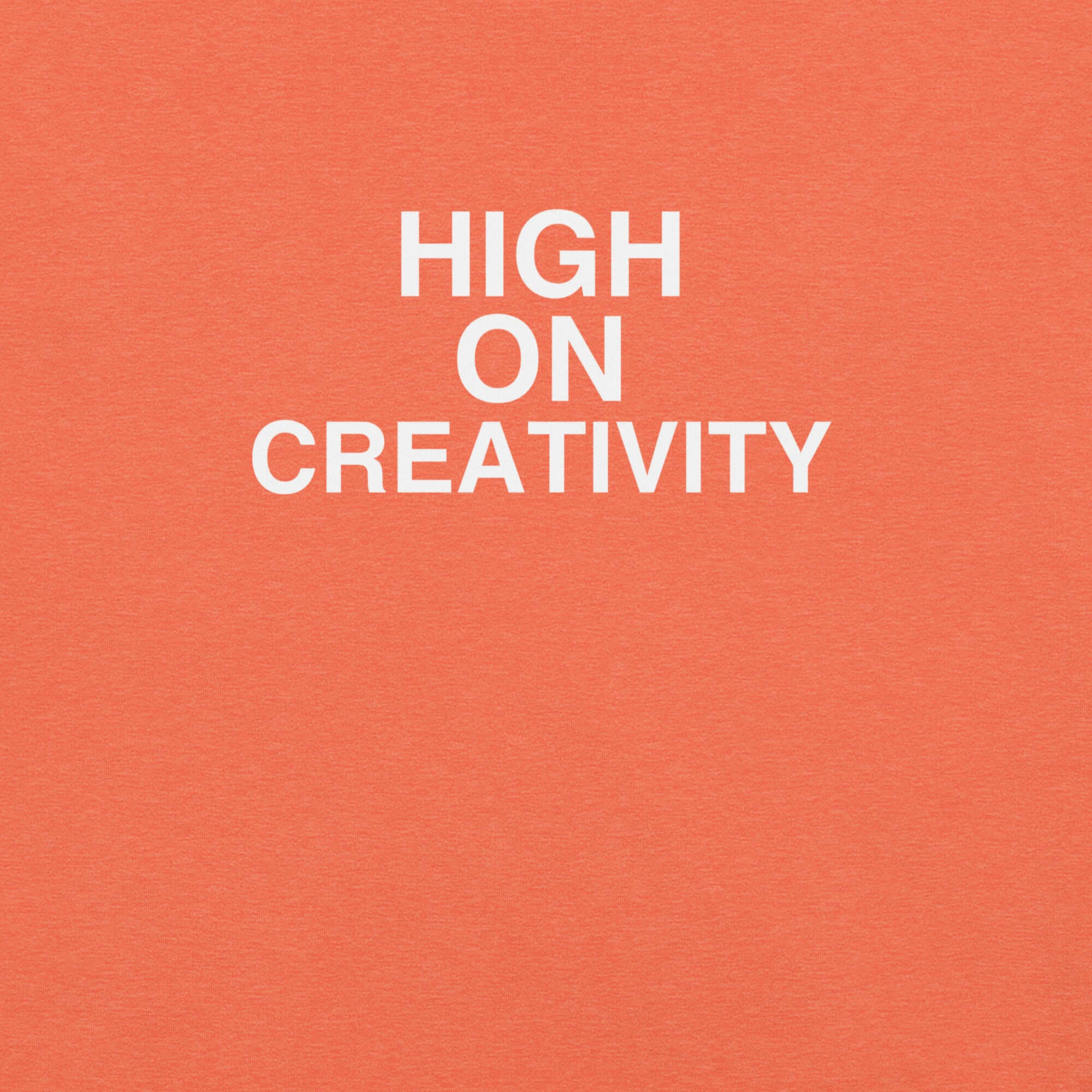 Close-up of orange t-shirt fabric with the phrase “HIGH ON CREATIVITY” printed in bold white uppercase letters in three lines.