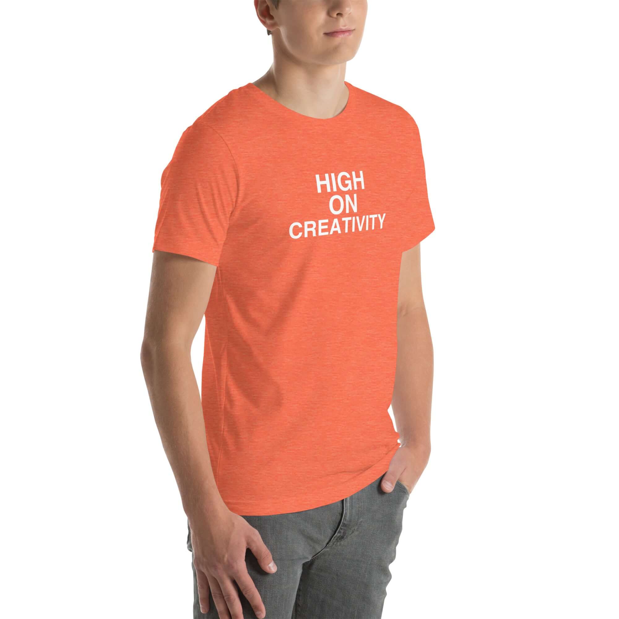 Young man wearing a orange t-shirt with white text ‘HIGH ON CREATIVITY’, standing angled to the side with hands in pockets.