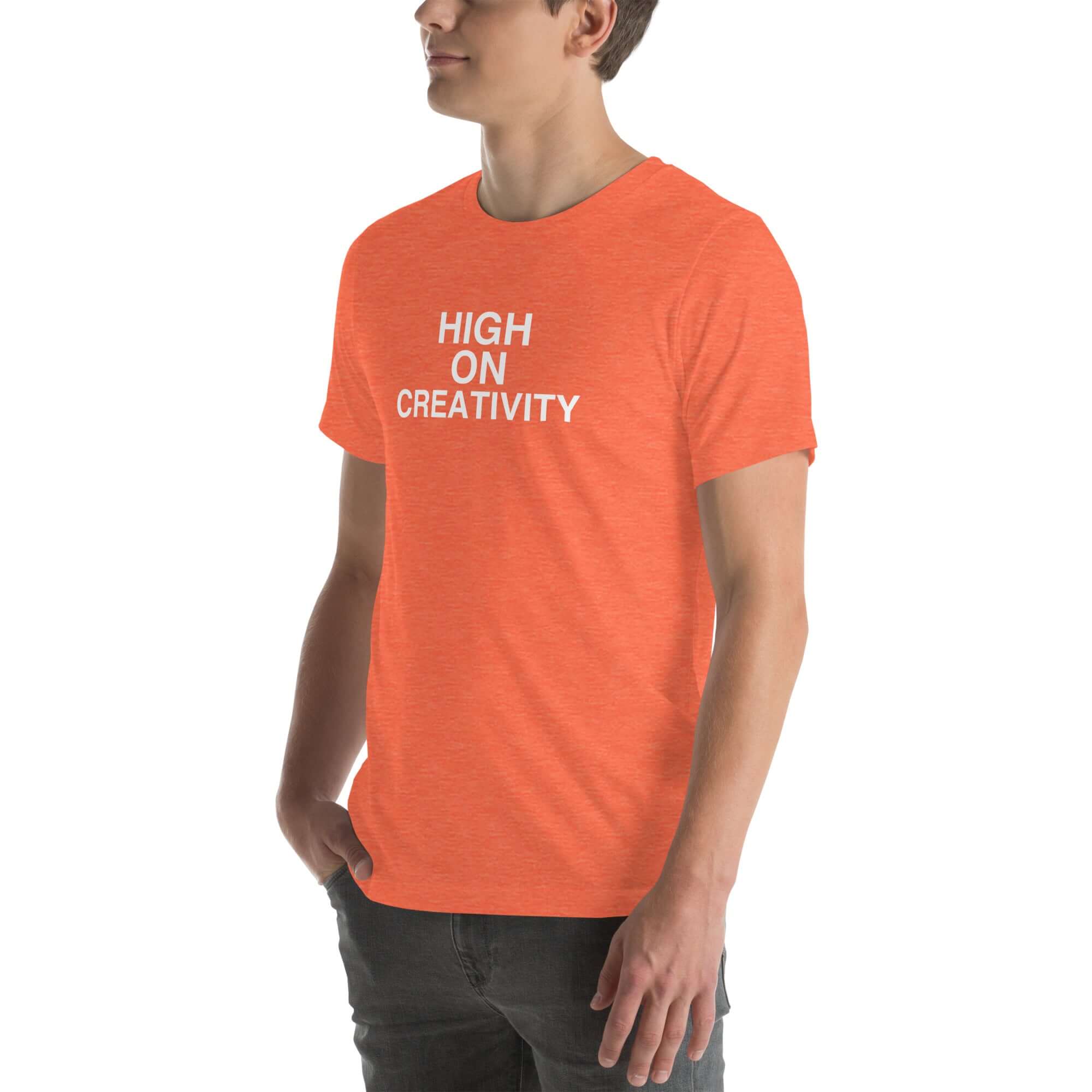 Man wearing a orange t-shirt with white text ‘HIGH ON CREATIVITY’, standing sideways with one hand in pocket