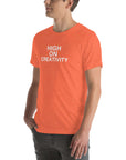 Man wearing a orange t-shirt with white text ‘HIGH ON CREATIVITY’, standing sideways with one hand in pocket