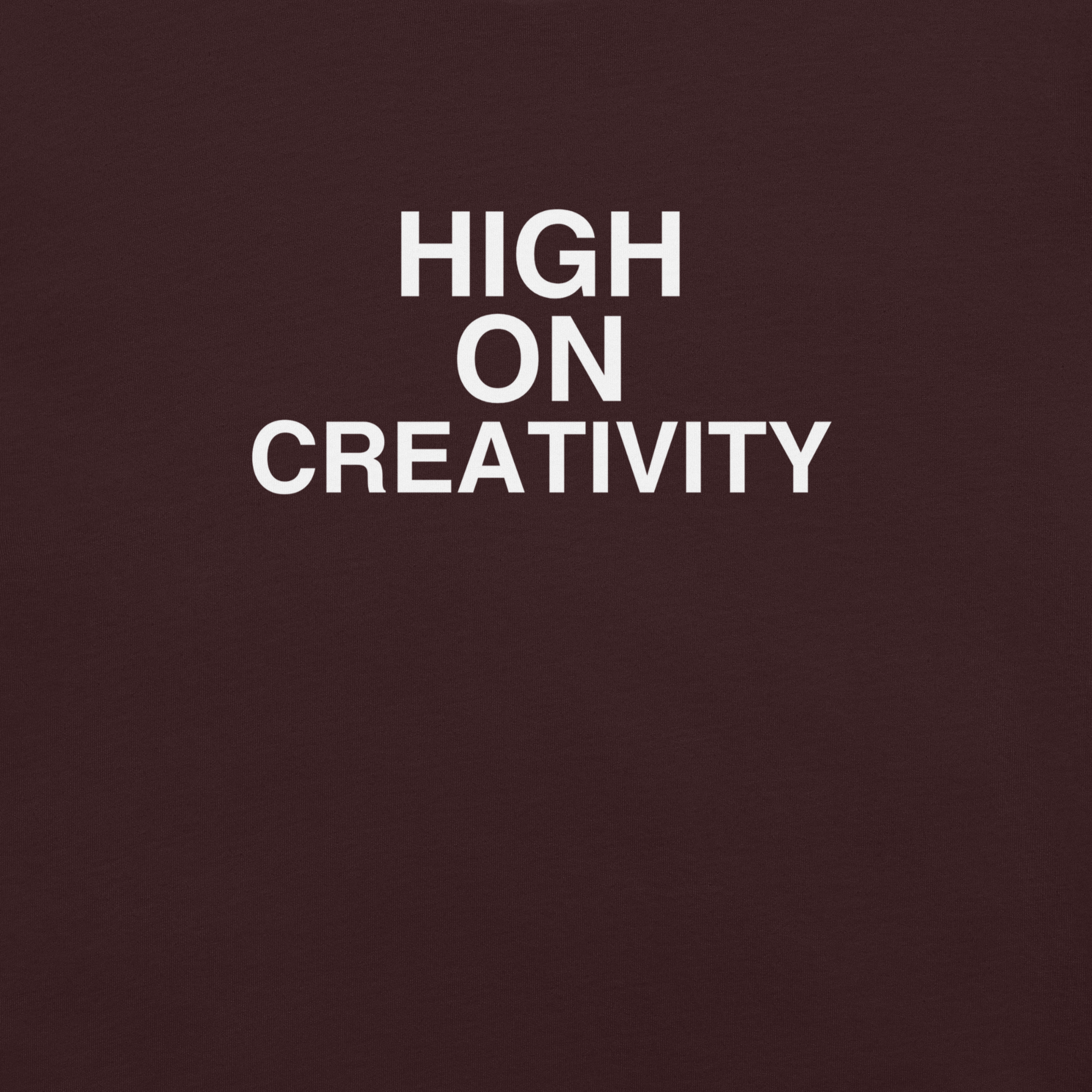 Close-up of oxblood black t-shirt fabric with the phrase “HIGH ON CREATIVITY” printed in bold white uppercase letters in three lines.