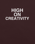 Close-up of oxblood black t-shirt fabric with the phrase “HIGH ON CREATIVITY” printed in bold white uppercase letters in three lines.