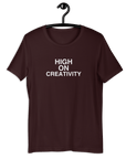 Oxblood black t-shirt on a hanger with the phrase “HIGH ON CREATIVITY” printed in white, centered on the chest.