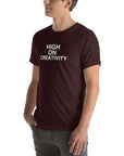 Man wearing a oxblood black  t-shirt with white text ‘HIGH ON CREATIVITY’, standing sideways with one hand in pocket