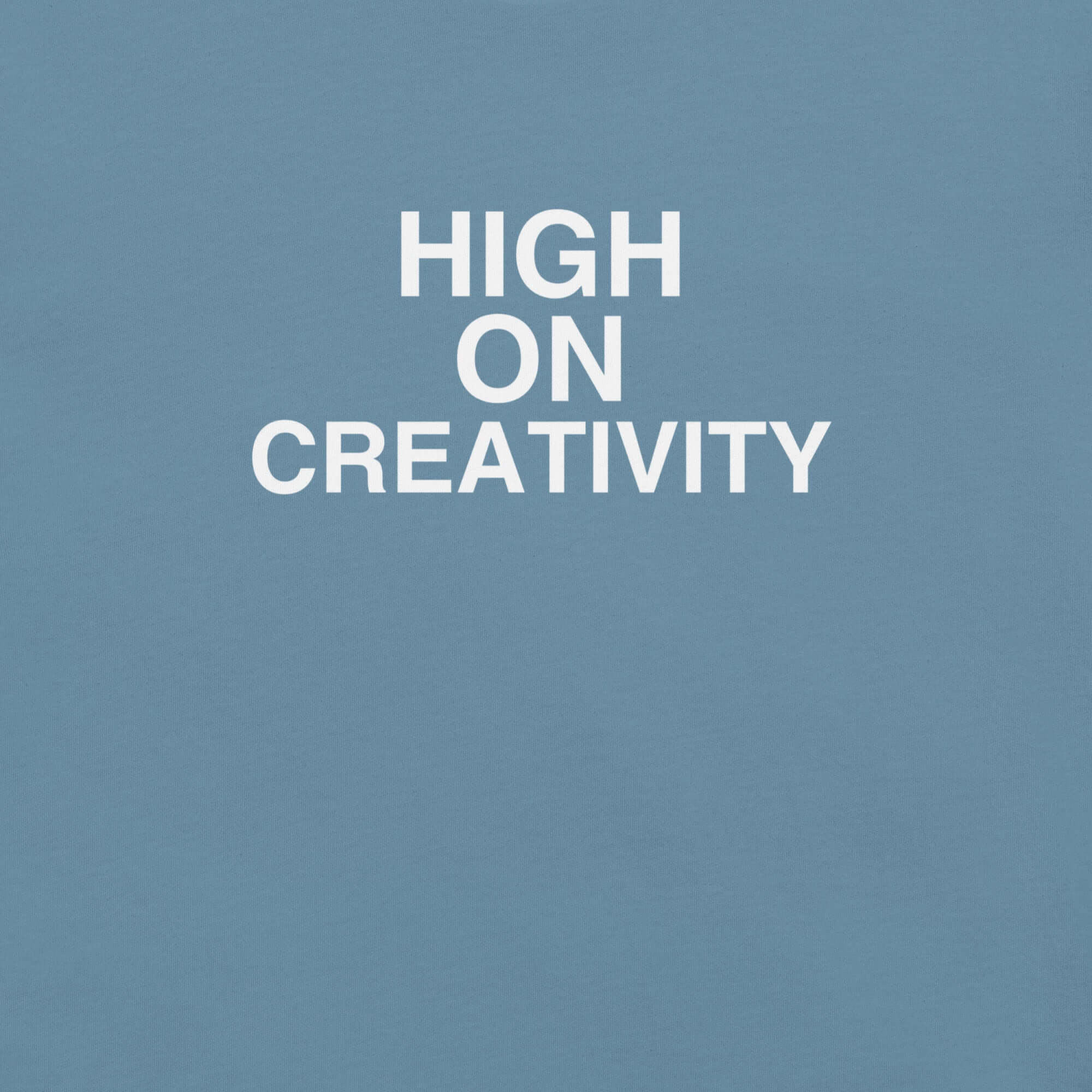 Close-up of steel blue t-shirt fabric with the phrase “HIGH ON CREATIVITY” printed in bold white uppercase letters in three lines.