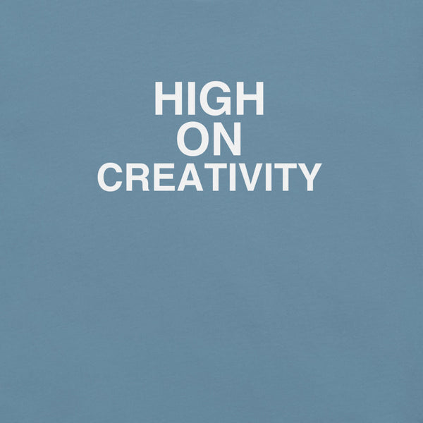 Close-up of steel blue t-shirt fabric with the phrase “HIGH ON CREATIVITY” printed in bold white uppercase letters in three lines.