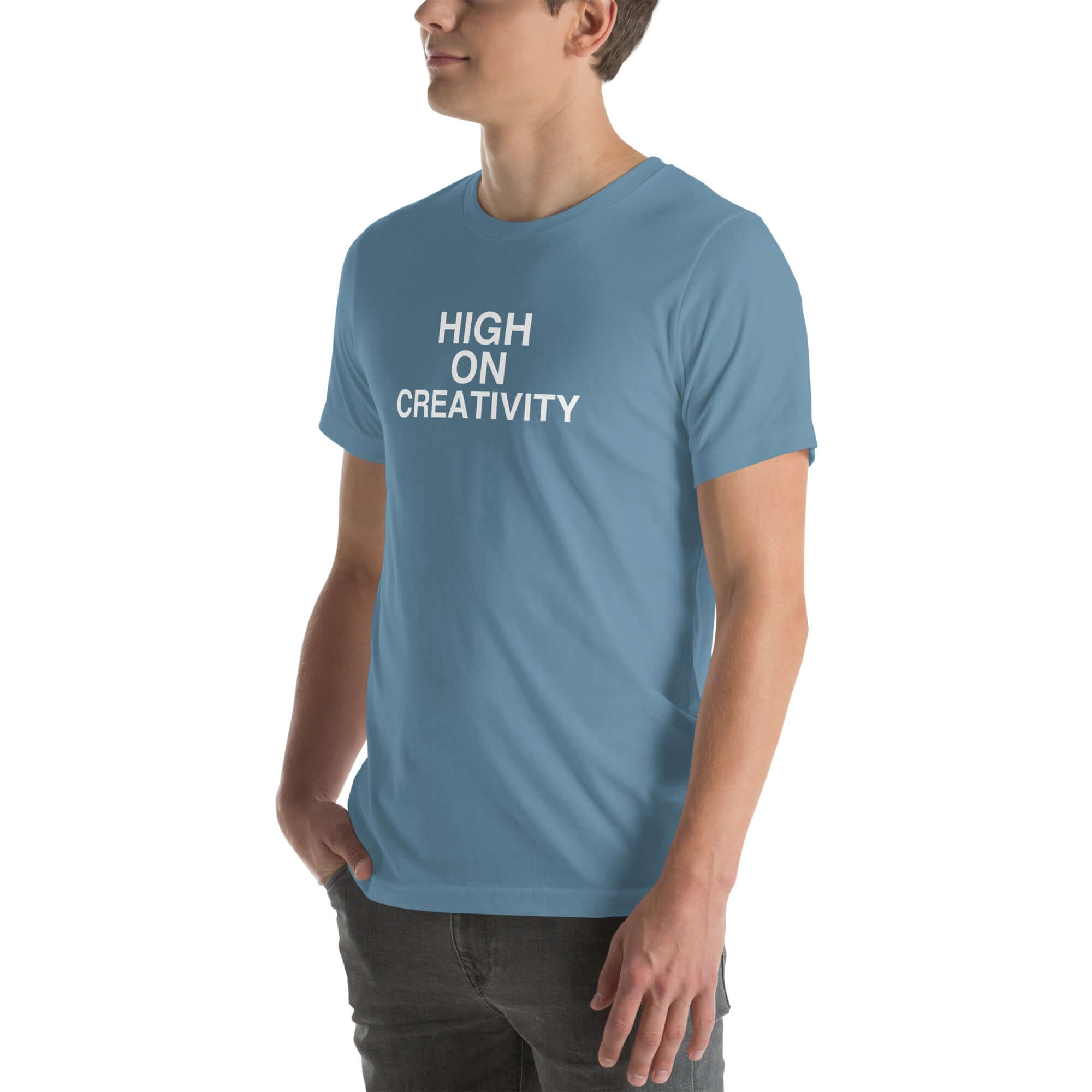 Man wearing a steel blue t-shirt with white text ‘HIGH ON CREATIVITY’, standing sideways with one hand in pocket