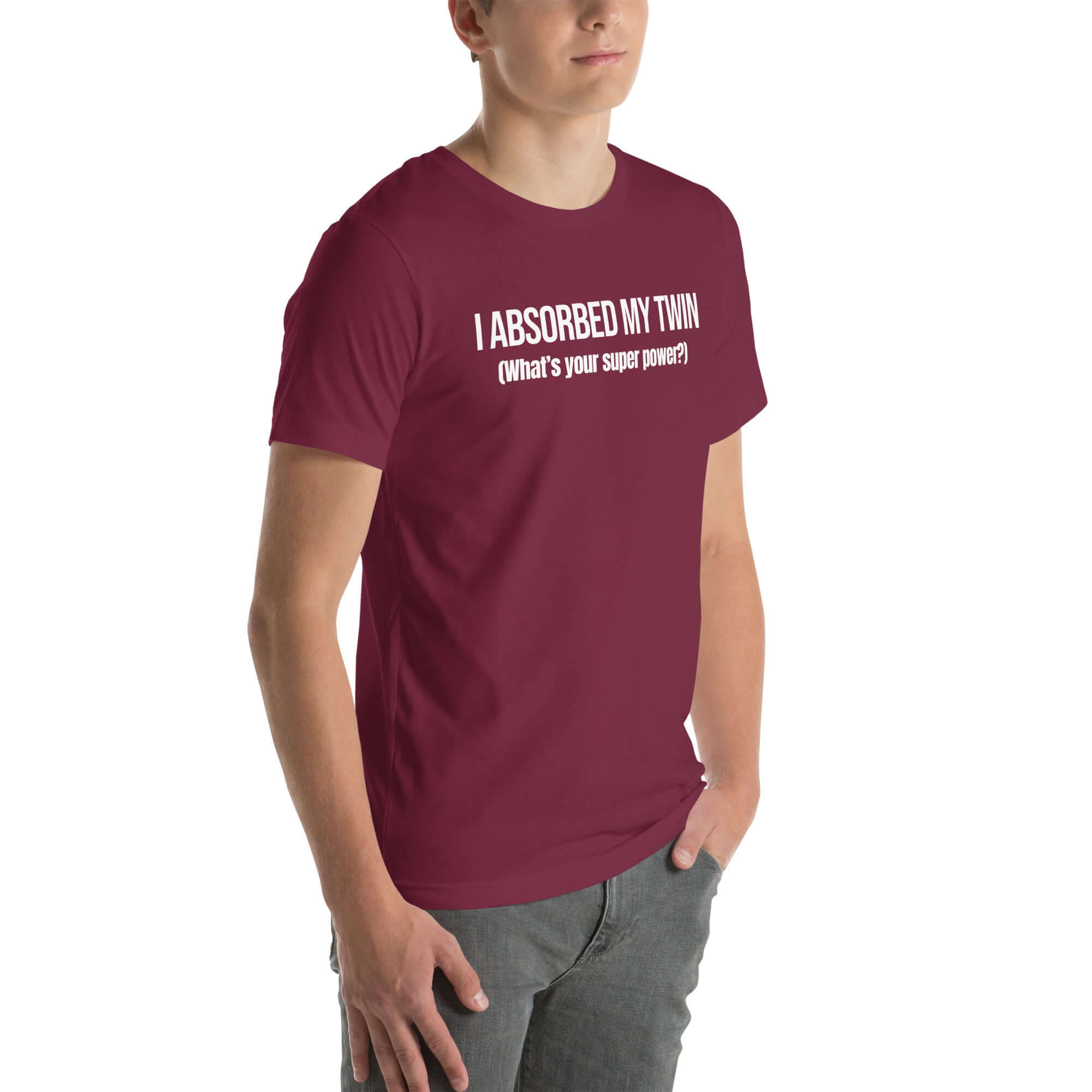 Man wearing maroon “I ABSORBED MY TWIN (What’s your super power?)” t-shirt, standing angled to the side with hands in pockets.