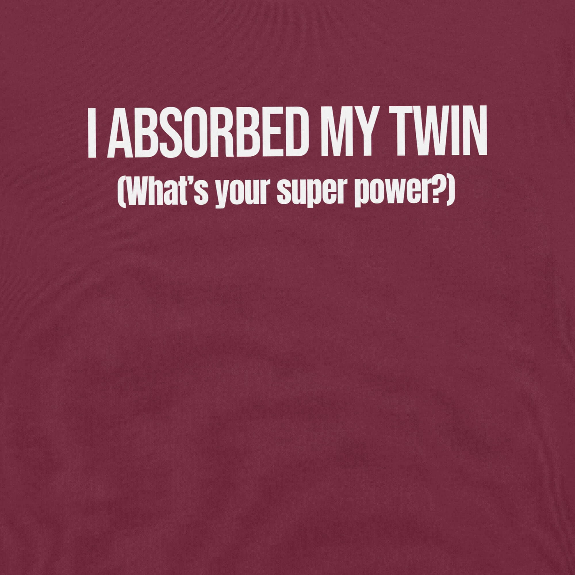 Close-up of maroon t-shirt with white text “I ABSORBED MY TWIN (What’s your super power?)” printed on the front.