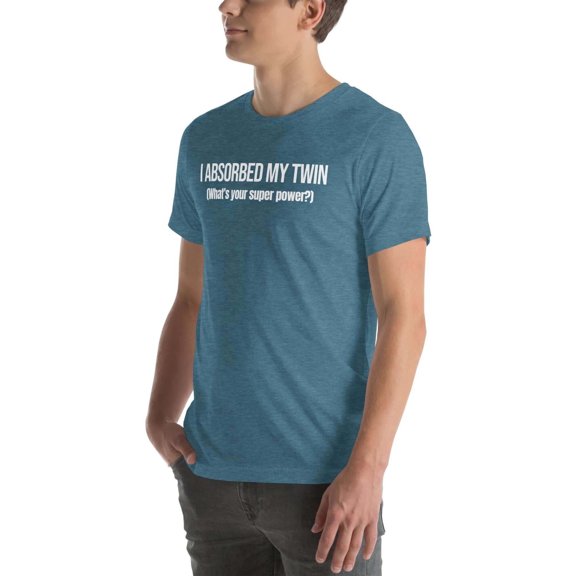 Man wearing teal “I ABSORBED MY TWIN (What’s your super power?)” t-shirt, standing sideways with hands in pockets.
