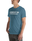 Man wearing teal “I ABSORBED MY TWIN (What’s your super power?)” t-shirt, standing sideways with hands in pockets.
