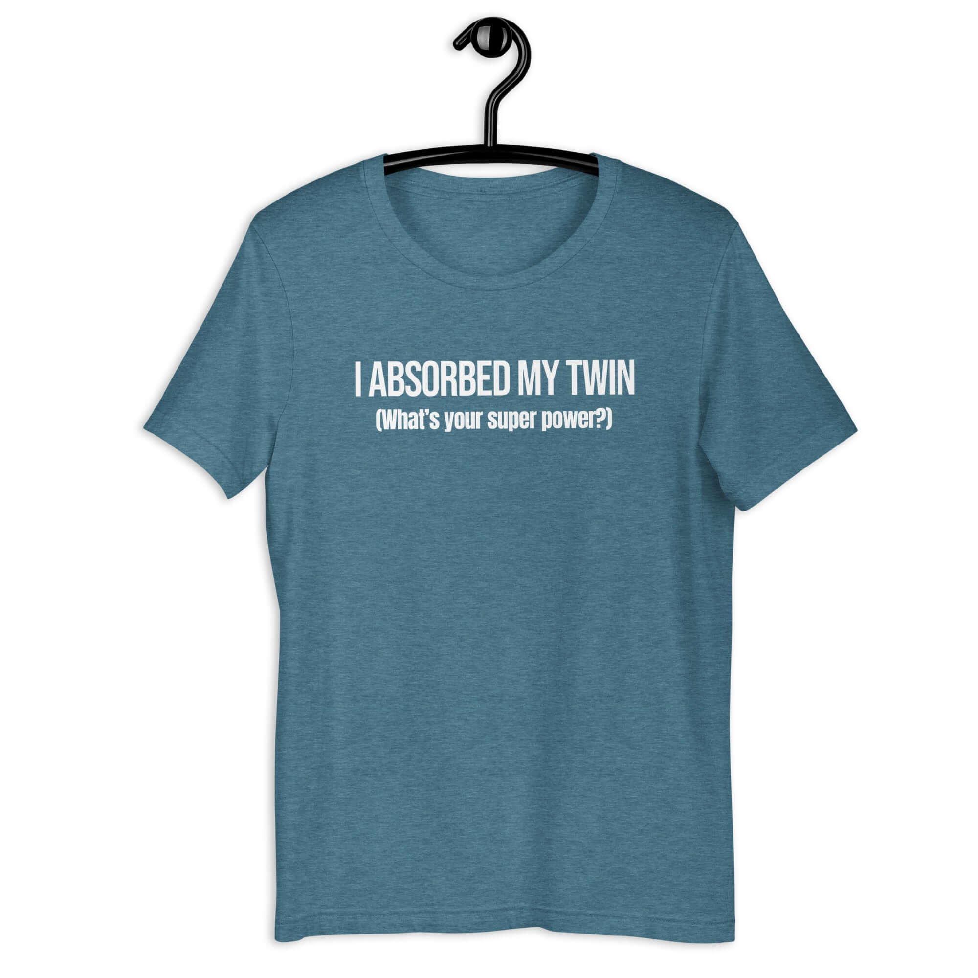 Teal t-shirt hanging on a hanger with white text “I ABSORBED MY TWIN (What’s your super power?)” on the front.         