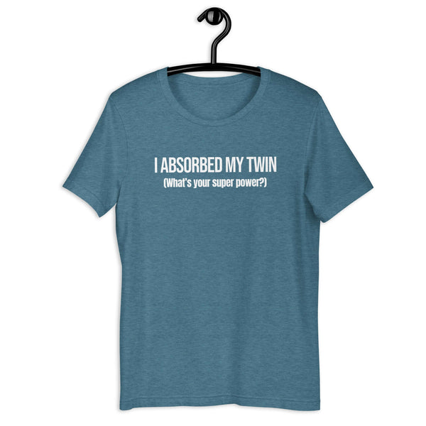 Teal t-shirt hanging on a hanger with white text “I ABSORBED MY TWIN (What’s your super power?)” on the front.         