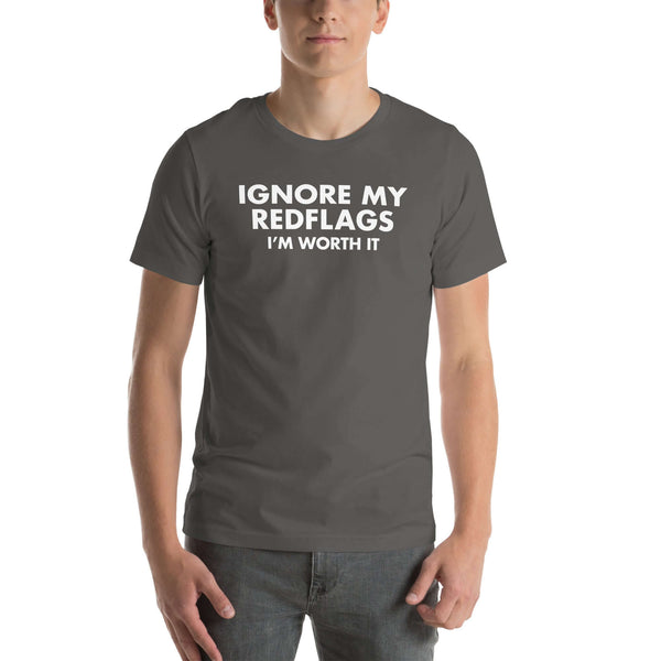 Man wearing asphalt “IGNORE MY RED FLAGS I’M WORTH IT” t-shirt, standing casually with hands by pockets.